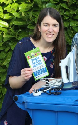 Louise holding a recycling leaflet standing next to a blue recycling bin